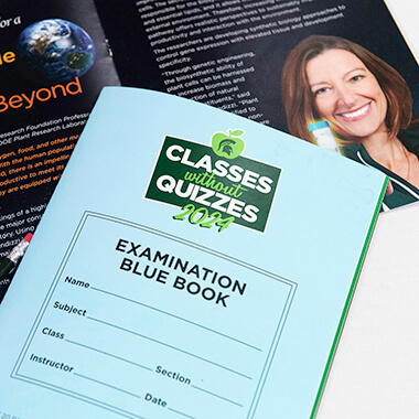 The printed program from the 2024 Classes Without Quizzes event was designed to look like a blue book for college exams. A closed copy of the program sits on a table showing that the cover reads “Classes Without Quizzes 2024” and has a spot to write a student’s name, subject, class, section, instructor and date. Behind it, a copy of the program is opened to a page featuring presenter Federica Brandizzi and shows how some of her work is helping prepare plants that astronauts can grow on space flights. 