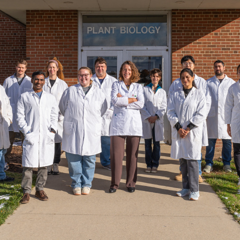 group photo of a professor with students in lab coats outside the plant biology building