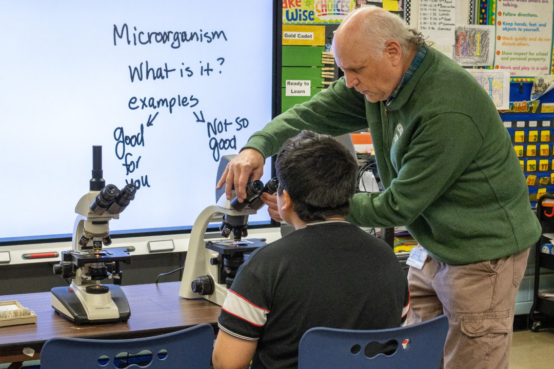 teacher helping a student use a microscope