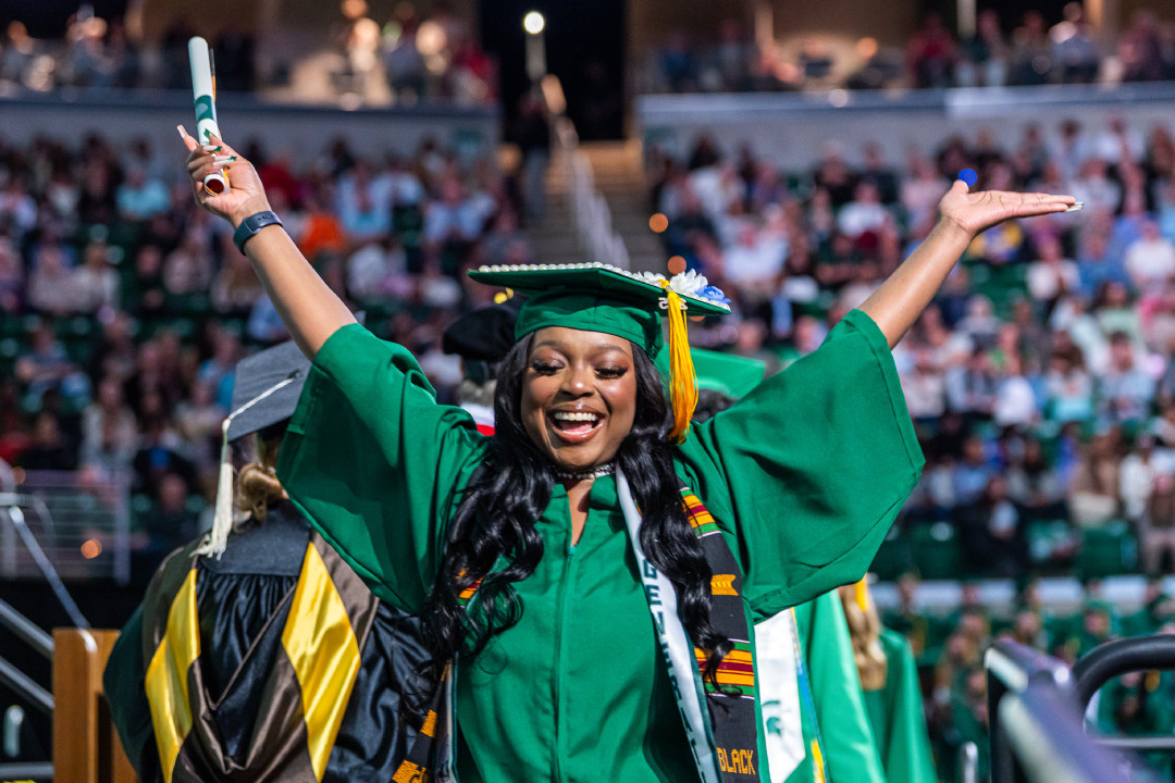 Student throwing hands in the air celebrating at graduation dressed in a cap and gown