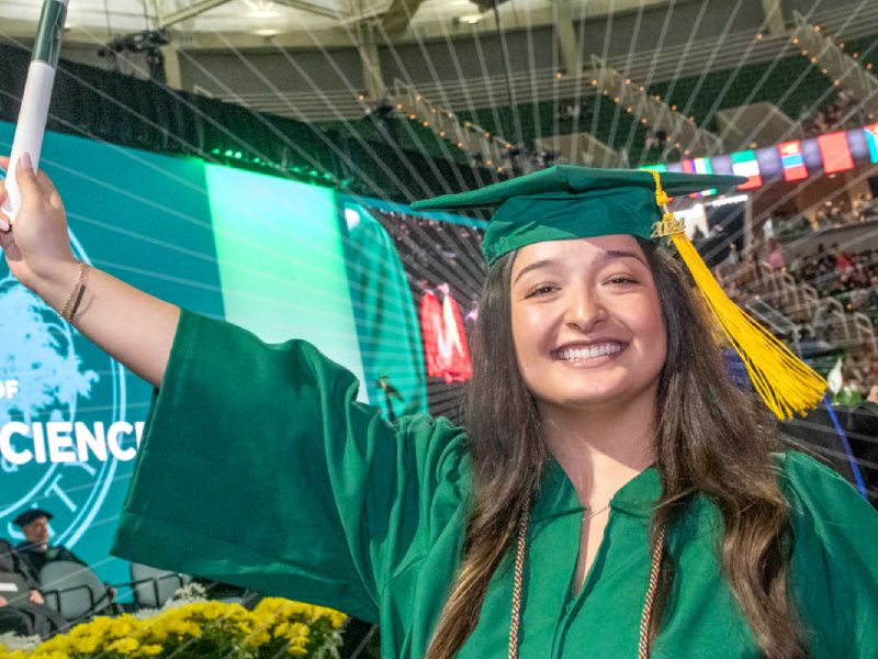 Student smiling at graduation holding up diploma