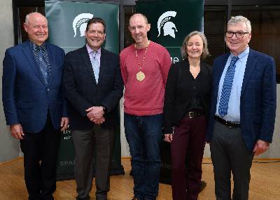 Sean Crosson (center) poses with investiture speakers up by the podium following the ceremony (L to R): Phil Duxbury, dean, College of Natural Science; Victor DiRita, chair, Department of Microbiology and Molecular Genetics; Birgit Puschner, dean, College of Veterinary Medicine; and Doug Gage, vice president, Office of Research and Innovation at MSU.