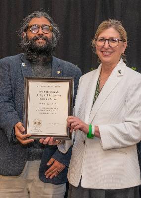 Jaideep Taggart SIngh posing with MSU Interim President Teresa Woodruff with his Donald F. Koch Quality in Undergraduate Teaching Award plaque.