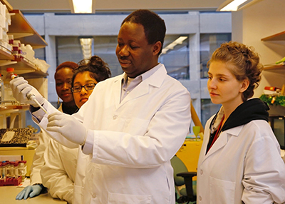 Seun Ogunwobi pictured in his lab demonstrating how to prepare a sample to a group of trainees.