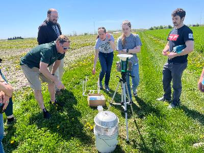 MSU XPRIZE Rainforest team members out in a field on campus examining a tripod equipped with motion-detecting cameras and microphones and other equipment that will be drone dropped into the Singapore rainforest.