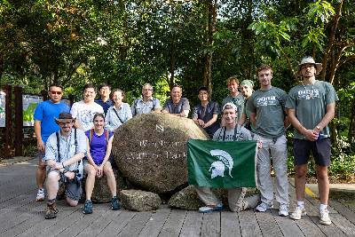 Groups shot of XPRIZE group members holding a Spartan flag next to a stone signage that says Windsor National Park.