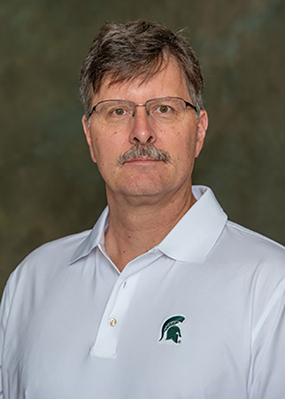 Headshot of MSU researcher Jeffrey Freymueller. He is wearing a white short-sleeved polo shirt with a Spartan helmet logo on the upper left side of his shirt.