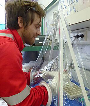 Dalton Hardisty works with scientific samples inside a glove bag, which is like a small, clear plastic tent designed to keep air from reaching the samples inside. Hardisty is able to handle the samples by placing his hands in large white gloves built into the side of the bag.