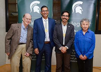 Aman Yadav (center left) and Danny Caballero (center right) pose in front of two College of Natural Science banners with Peter Lappan (left) and Betty Phillips (right) following their investiture ceremony. 