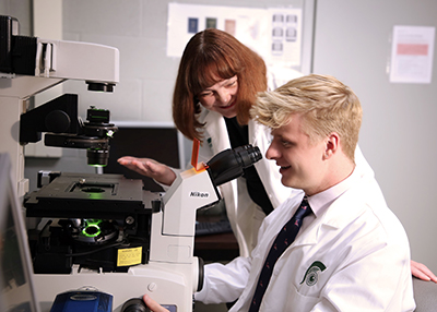 Professor Julia Busik watches on as Doctoral candidate Tim Dorweiler looks at retina tissue under a microscope.