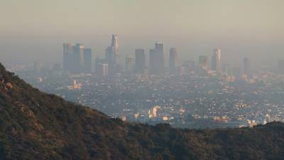 The skyscrapers of Los Angeles appear hazy in the distance due to brownish orange smog. A slope of Mount Hollywood is seen in the foreground.