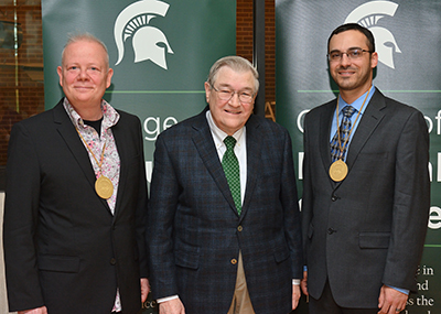 Bjoern Hamberger (left) and Ben Orlando (right) pose with Dr. James K. Billman, Jr., following their investiture ceremony in front of two vertical College of Natural Science banners.. 