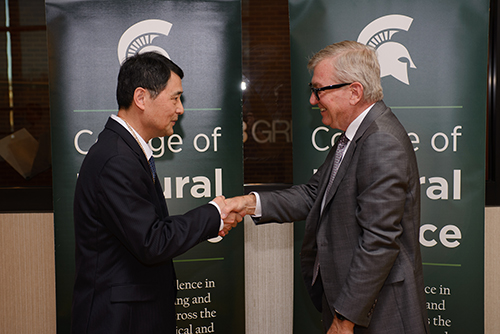 MSU Research Foundation Professor Guowei Wei and Vice President of Research and Innovation Doug Gage shaking hands as Gage presents Wei with a medal.