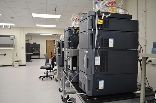 Boxy gray and black instruments sit on tabletops in the newly renovated Mass Spectrometry and Metabolomics Core facility. Reagent bottles rest on top of the instruments and are connected to the machines with thin plastic tubing.