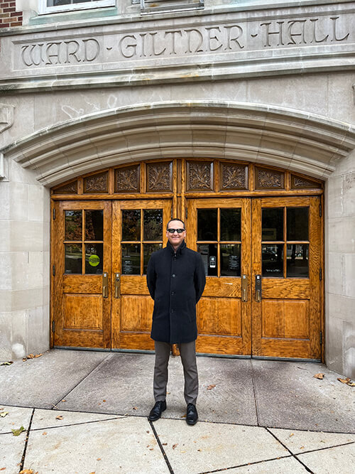 Kevin McGraw stands in front of the wooden doors and stone façade of Ward Giltner Hall.