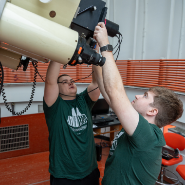 Two Michigan State University students adjust a camera on a research telescope.