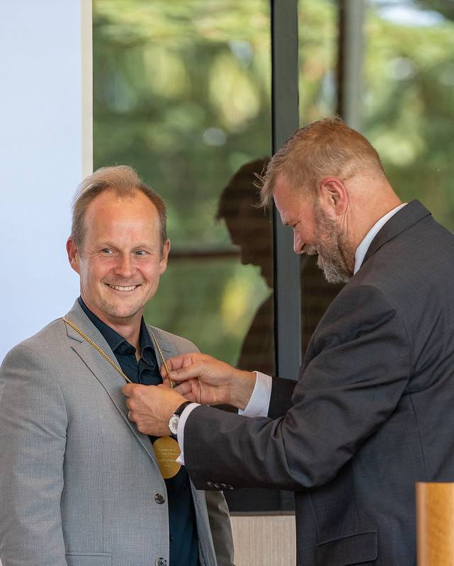 MSU interim provost wearing a suit hangs a medallion around the neck of MSU physicist.