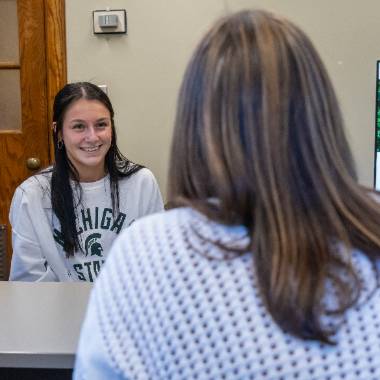 A student sits at a desk smiling at her pre-health advisor.