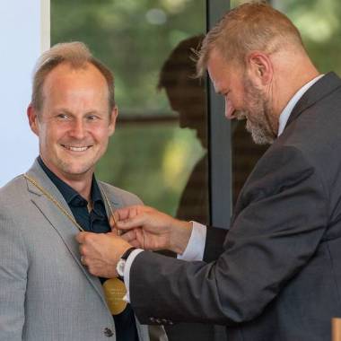 An MSU interim provost wearing a suit hangs a medal around the neck of MSU physicist Johannes Pollanen.