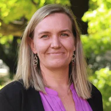 This is a picture of Vashti Sawtelle, a blond woman in a purple shirt and blazer standing outside