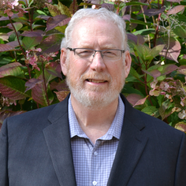 A man in a suit stands in front of flowers