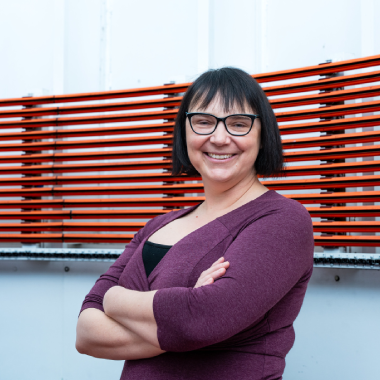 A woman smiles with her arms crossed in front in an observatory telescope room.