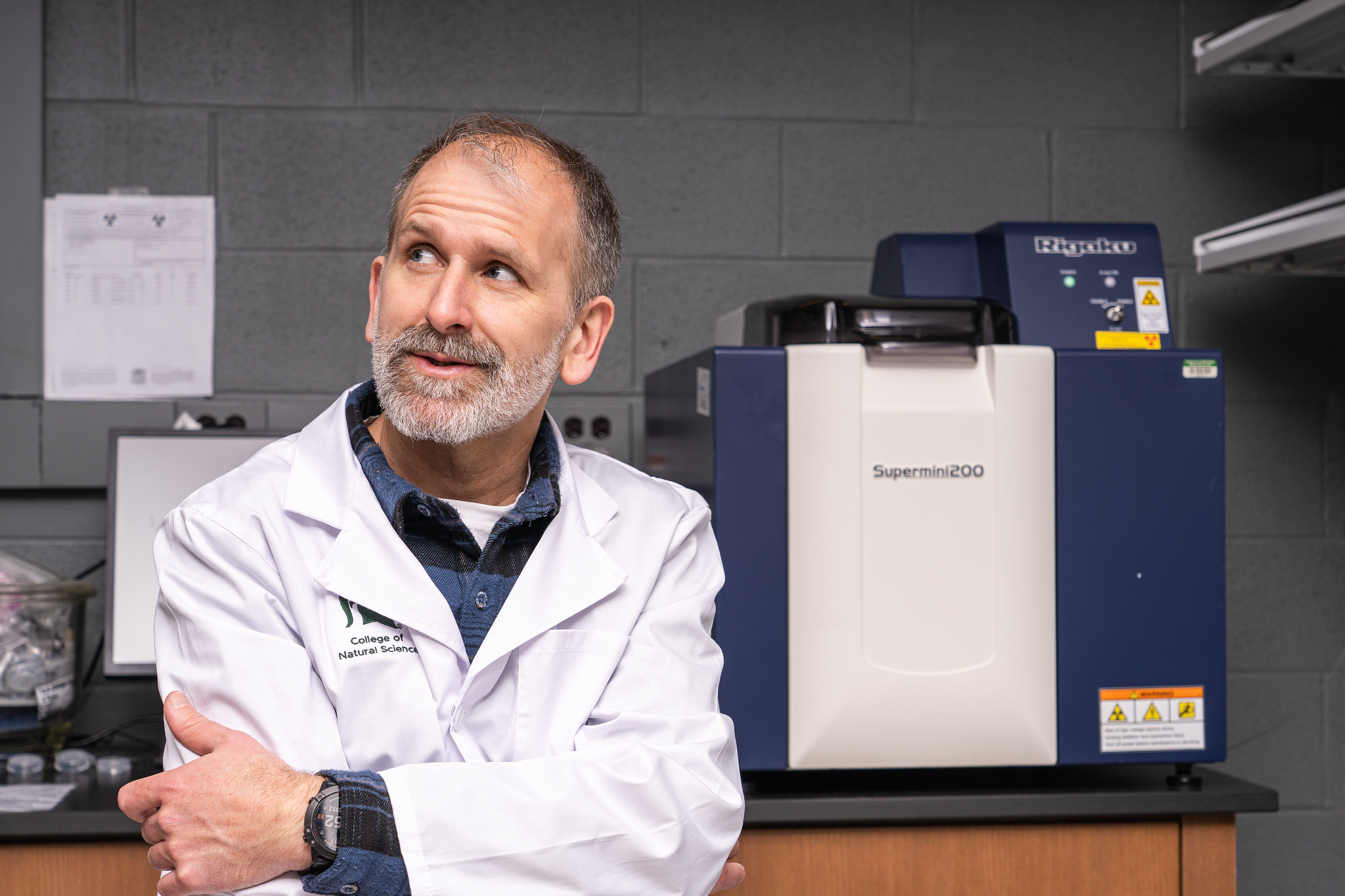 Tyrone Rooney, wearing a lab coat, sits in lab discussing rock chemistry