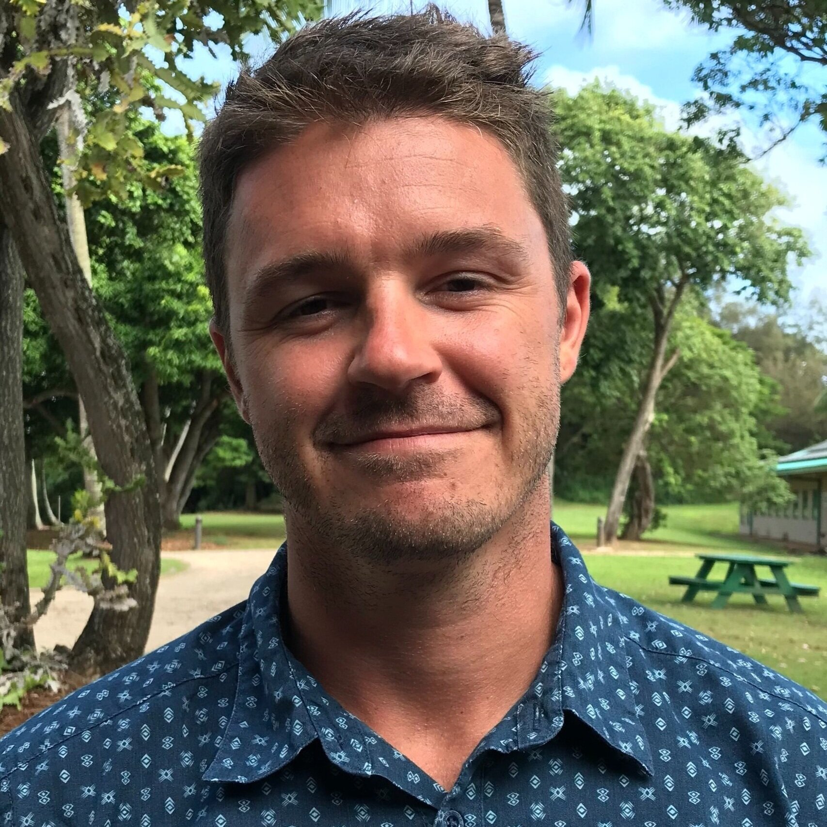 Headshot of Crawford Drury who wears a dark and light blue button down shirt against greenery.