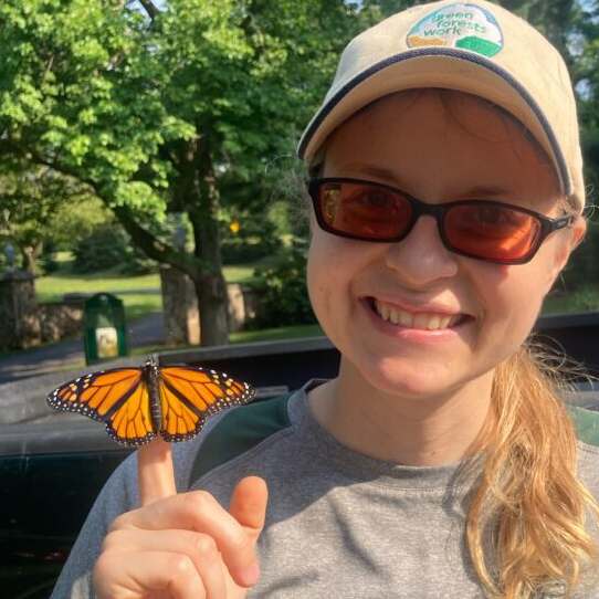Wendy Leuenberger smiles at camera while holding a monarch butterfly on her finger