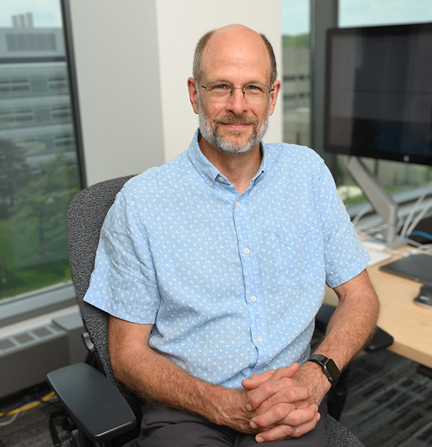 Karl Olson sits on a chair next to a desk.