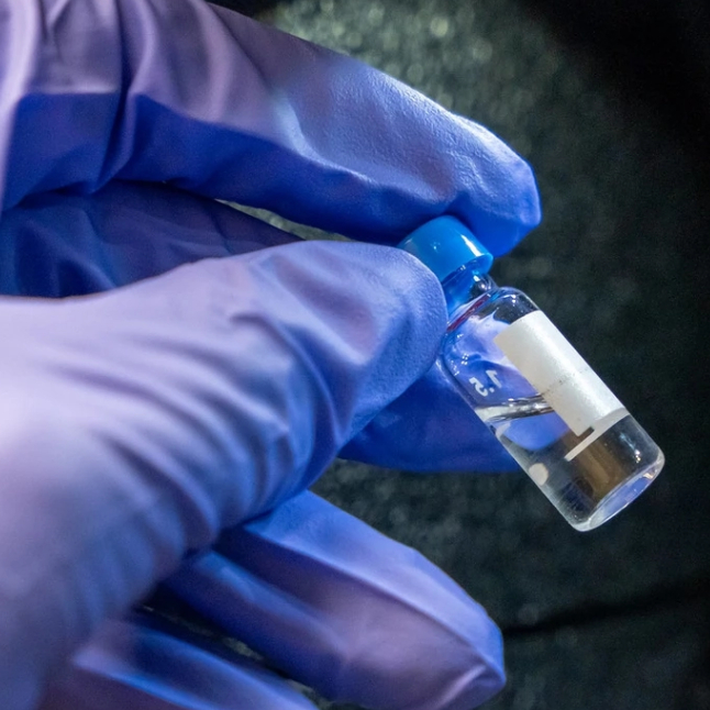 blue gloved hand holds a small phial 