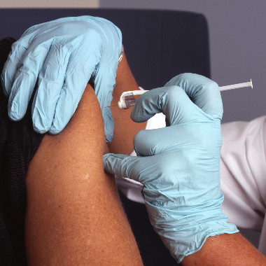 Gloved hands holding a syringe hover above an arm about to receive a shot.