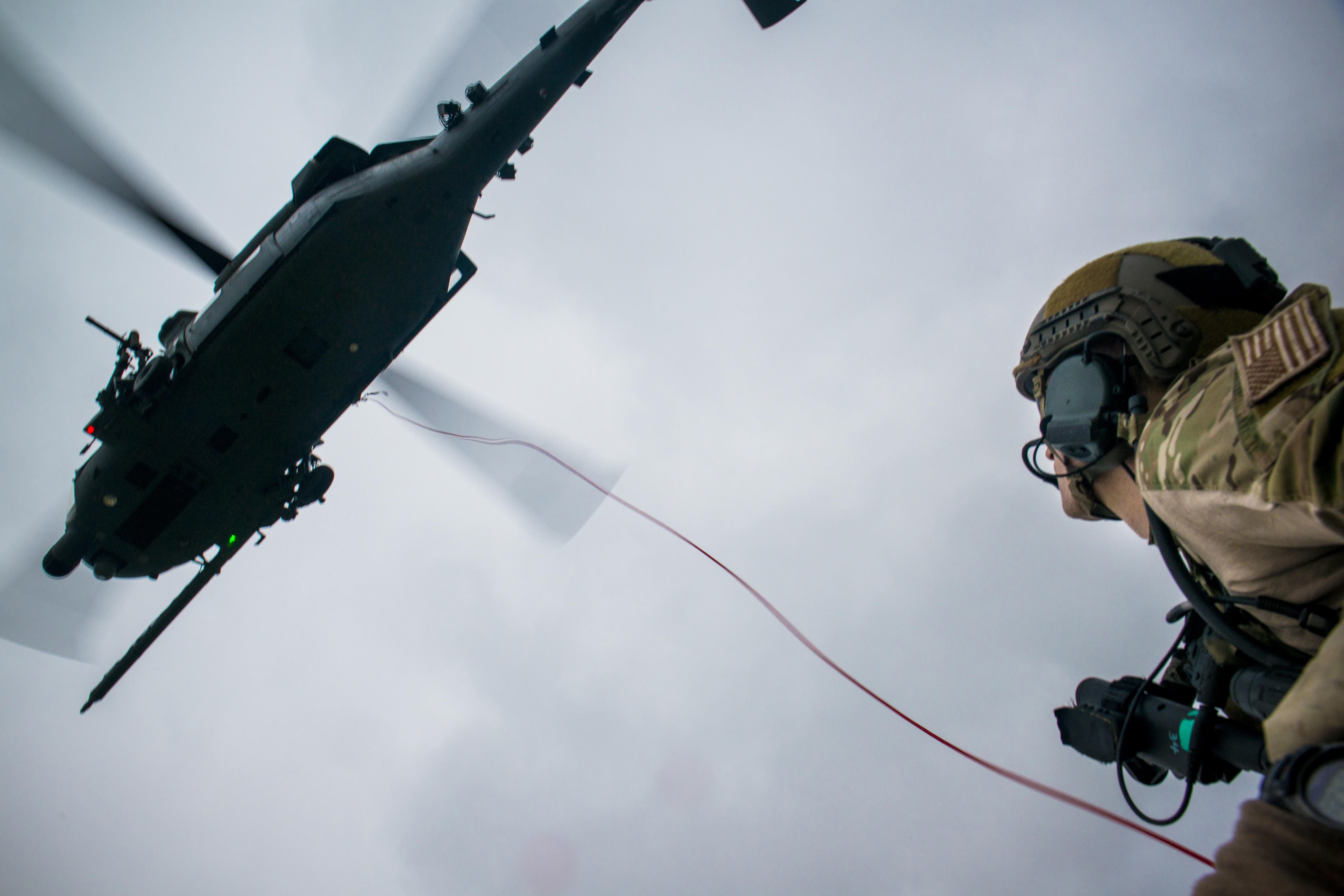 A military operative hangs from a helicopter.
