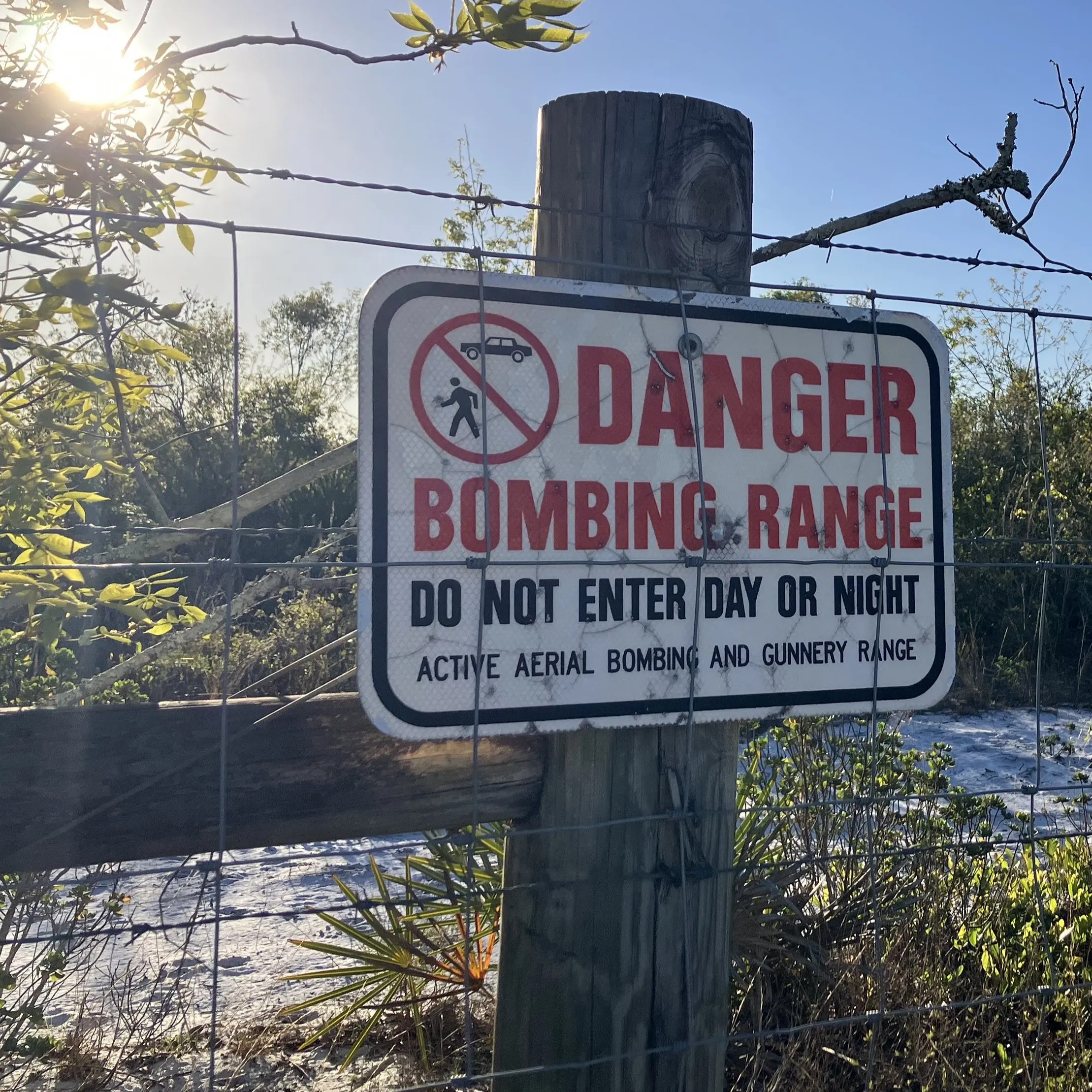 A sign attached to a wooden post, surrounded by barbed wire. The sign warns readers not to enter the area ahead as it is a bombing range.