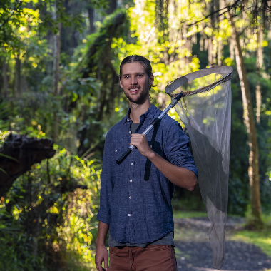 A young man stands in a forest with a butterfly net.