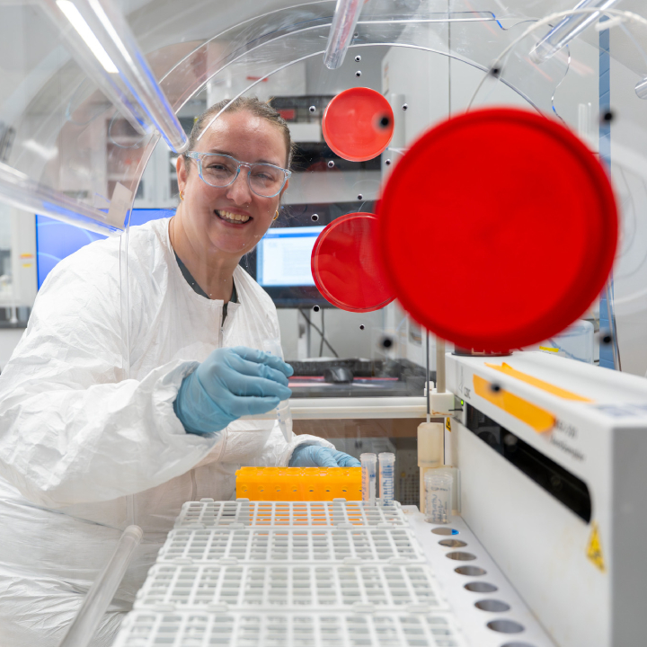 A scientist in a clean room suit and goggles looks through a machine.