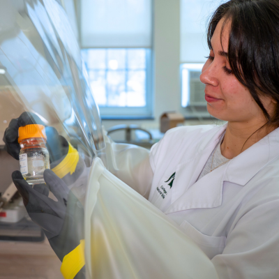 A scientist holds a bottle in an anaerobic chamber.