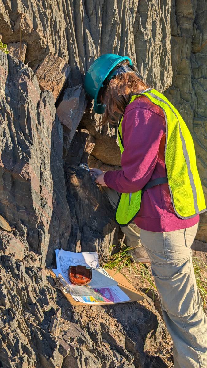 student works on collecting a sample from a rock formation