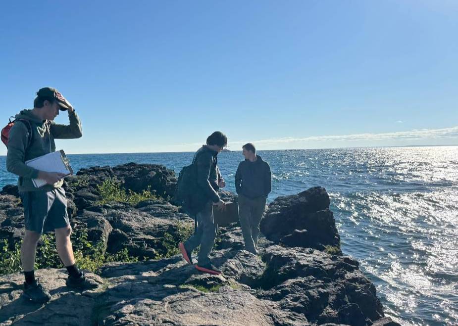 Students stand on rock formation next to a body of water
