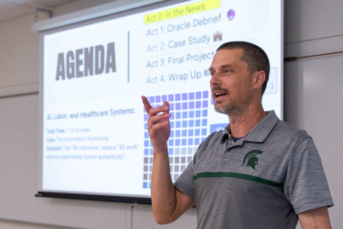 faculty member stands in front of screen projected with an Agenda slide