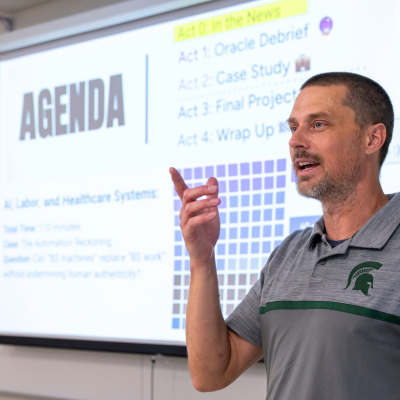 Faculty member stands in front of a screen projected with an Agenda slide