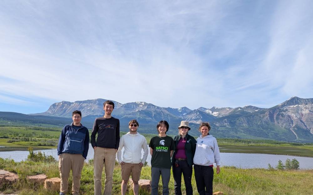 6 people stand in a line in front of a mountain range