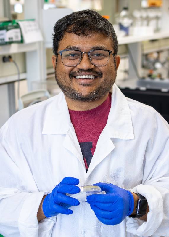 head and shoulders profile photo of Ritam Sinha.  He wears a white lab coat and blue latex gloves.
