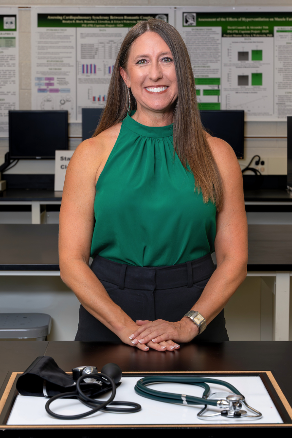 Woman with long dark brown hair stands in front of a wall covered in scientific presentation posters