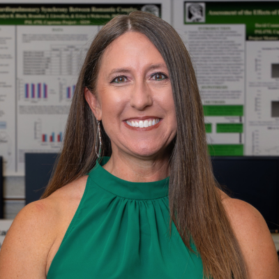 Woman with dark brown hair and green halter top stands in front of a wall of scientific posters.