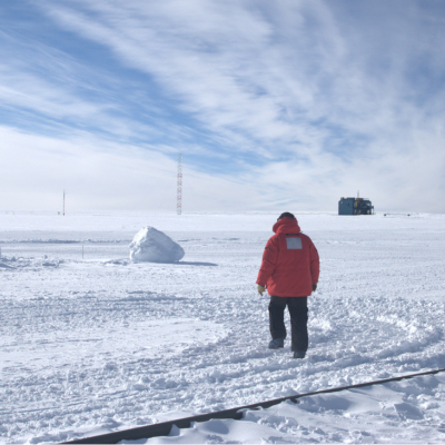 A man in an orange park walks in snow at the South Pole
