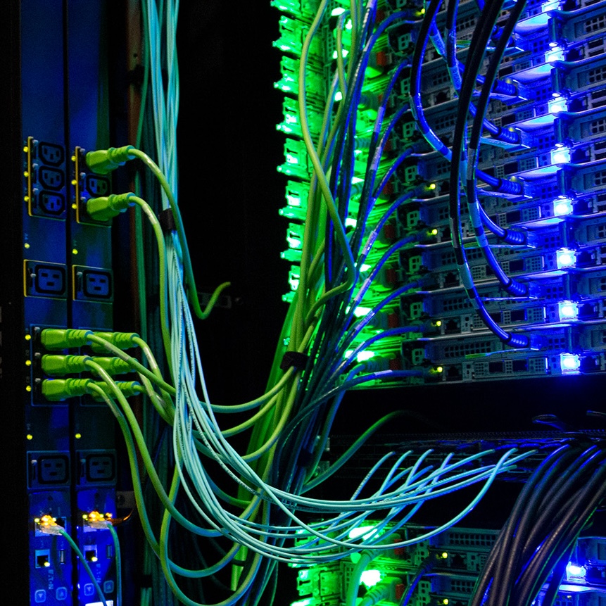Wires criss-cross a server rack illuminated blue and green