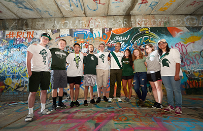 A photo displaying NatSci students in a group under a bridge with graffiti behind them.