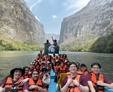 group of students rafting on a river with a mountain in the background