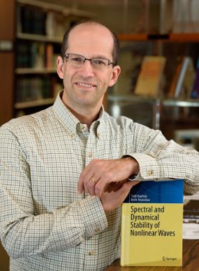 Keith Proislow poses with a math book that he co-authored on spectral and dynamical stability of nonlinear waves.